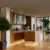 A modern, well-lit kitchen with wooden cabinets, an island, and a large window overlooking an outdoor space. Produktbild-Vorschau