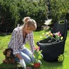 A woman is gardening in a yard with her dog nearby, using a garden cart. Podgląd zdjęcia produktu