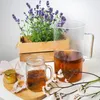 A pitcher of iced tea, a jar of honey, and a pot of lavender are arranged on a wooden board. Produktbild-Vorschau