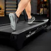 A person's legs and feet are shown running on a black treadmill in a gym setting. Produktbild-Vorschau