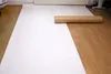 A large roll of white paper is laid out on a wooden floor, with a brown cardboard tube lying on top of it. Produktbild-Vorschau