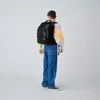 A person wearing a backpack and jeans, standing against a white background. Produktbild-Vorschau
