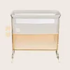 A baby crib with mesh sides and a beige and orange color scheme, presented on a light beige background. Produktbild-Vorschau