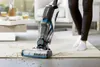 A person is using a Bissell CrossWave vacuum cleaner on a rug in a living room. Produktbild-Vorschau