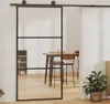 A sliding glass door with a black frame is shown in a room with wooden floors. A dining table and chairs are visible through the glass, and a potted plant is in the foreground. Podgląd zdjęcia produktu
