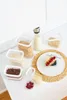 A collection of food storage containers filled with various breakfast ingredients, including cereal, raisins, and berries, along with a bottle of milk, arranged on a white surface with a placemat and plate. Náhľad obrázku produktu