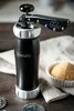 A black biscuit press with silver accents sits on a wooden surface next to a bowl of brown sugar and a linen cloth. Anteprima dell’immagine prodotto