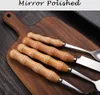 A close-up view of four cutlery pieces with wooden handles resting on a wooden cutting board. Voir les images du produit