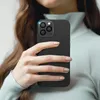 A person holding a black smartphone with a camera lens protector. Produktbild-Vorschau