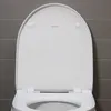 A close-up, top-down view of a white toilet seat with the lid up, showing the brand logo and hinges against a grey tiled wall. Produktbild-Vorschau