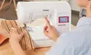 A person is using a Brother sewing machine to sew a piece of fabric. Produktbild-Vorschau