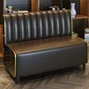 A brown leather sofa with gold trim is shown in a room with bookshelves in the background. Produktbild-Vorschau