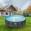 An above-ground pool with a rattan-like frame is set up on a green lawn in front of a modern house. Produktbild-Vorschau