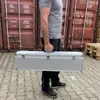 A person is holding a silver case in front of shipping containers. Produktbild-Vorschau