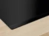 A close-up view of the edge of a black induction hob resting on a light wood surface. Anteprima dell’immagine prodotto