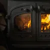 A close-up view of a burning wood stove with flames visible through the glass doors. Produktbild-Vorschau