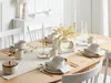A dining table set for four with plates, bowls, mugs, cutlery, and a vase with dried flowers. Náhľad obrázku produktu