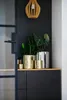 A collection of decorative planters with plants on a shelf against a dark wall, with a wooden pendant light above. Produktbild-Vorschau