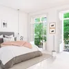 A bedroom with a bed, a balcony with greenery visible through open doors, and a floor-standing air purifier. Podgląd zdjęcia produktu