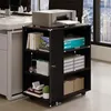 A dark wood printer stand with shelves, holding books, paper, and a cactus, next to a white desk in an office setting. Náhled obrázku produktu