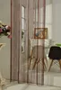 A string curtain hangs in front of a room divider with windows, revealing chairs and a table in the background. Produktbild-Vorschau
