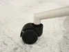 A close-up view of a black caster wheel attached to a light-colored leg of a chair, resting on a textured light gray surface. Anteprima dell’immagine prodotto