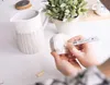 A person is decorating a small ceramic mug with a porcelain pen, next to a larger pitcher with a patterned design. Anteprima dell’immagine prodotto