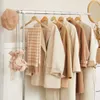A collection of neutral-toned coats hanging on a clothing rack, with a beret and a small bag displayed on the left. Podgląd zdjęcia produktu