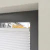 A close-up view of a white pleated blind in a window frame, with a street scene visible through the window. Produktbild-Vorschau