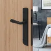 A black door handle set on a wooden door, with a bedroom scene in the background. Produktbild-Vorschau