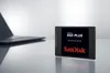 A SanDisk SSD Plus solid-state drive is placed on a reflective surface next to a laptop. Náhľad obrázku produktu