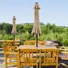 An outdoor patio scene with wooden tables and chairs, and two closed patio umbrellas. Produktbild-Vorschau