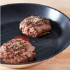 Two hamburger patties cooking in a grill pan with a dollop of ketchup. Produktbild-Vorschau