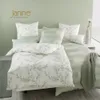 A neatly made bed with Janine brand bedding, set against a light green wall. Produktbild-Vorschau
