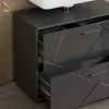 A close-up view of a dark grey vanity cabinet with geometric drawer fronts, a white sink on top, and a gold hook on the wall. Anteprima dell’immagine prodotto