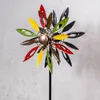 A colorful metal wind spinner shaped like a flower against a textured gray background. Produktbild-Vorschau