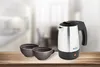 A travel kettle and two cups of coffee on a wooden table, with a blurred kitchen background. Produktbild-Vorschau