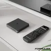 A black media streamer and remote control are placed on a light gray surface next to a television stand. Anteprima dell’immagine prodotto