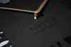 Close-up of a black wall clock with gold hands and embossed text. Anteprima dell’immagine prodotto