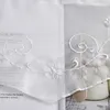 A close-up of white sheer fabric with embroidered floral and swirl patterns, layered over a book with text. Produktbild-Vorschau