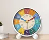 A colorful alarm clock is placed on a wooden surface in front of a light-colored wall. Produktbild-Vorschau