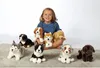 A young girl sits on a rug surrounded by several plush dog toys. Produktbild-Vorschau