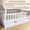 A white wooden bed with a safety barrier and drawers, with text overlays describing the safety barrier. Produktbild-Vorschau