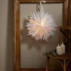 A white paper star lantern hangs in a wooden frame, with candles and greenery on a chair to the side. Podgląd zdjęcia produktu