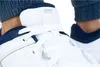 Close-up of a white Nike shoe with navy blue accents, worn by a person in blue pants. Voir les images du produit