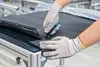 A person wearing protective gloves is using a utility knife to cut a piece of black material on a cutting mat. Voir les images du produit
