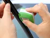 Hands cleaning a car windshield wiper blade with a green and white cleaning tool. Produktbild-Vorschau