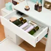 A drawer of a white vanity table is open, revealing various cosmetic bottles and containers. Voir les images du produit