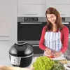 A woman in an apron is preparing food in a kitchen, with an air fryer in the foreground. Produktbild-Vorschau