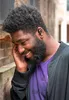 A man wearing earbuds and a purple t-shirt, smiling and touching his ear. Anteprima dell’immagine prodotto